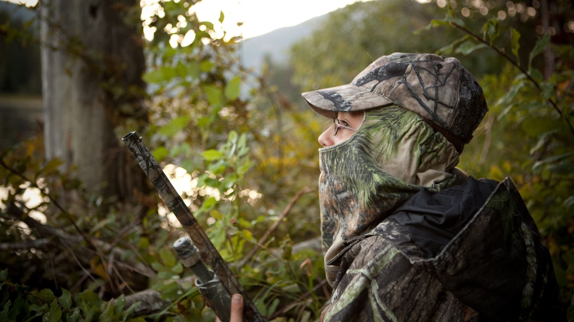 Hunter in camouflage gear observing forest, holding hunting rifle
