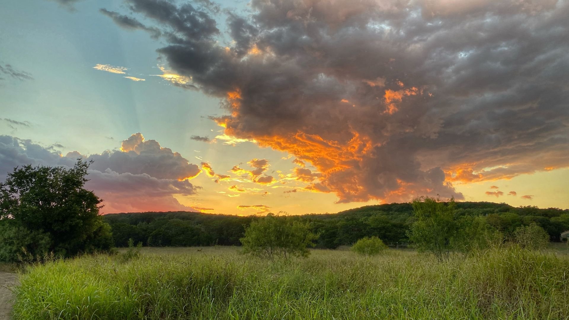 Dramatic sunset with orange clouds over green field and forested hills
