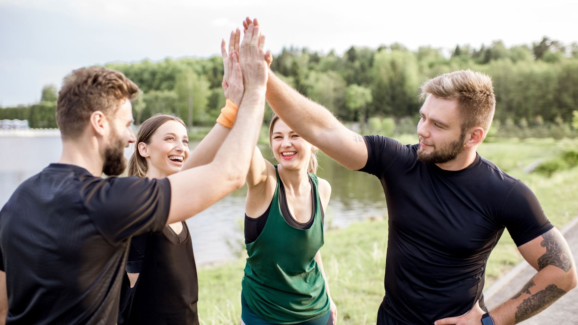 Friends giving high-fives outdoors, celebrating together near a lake